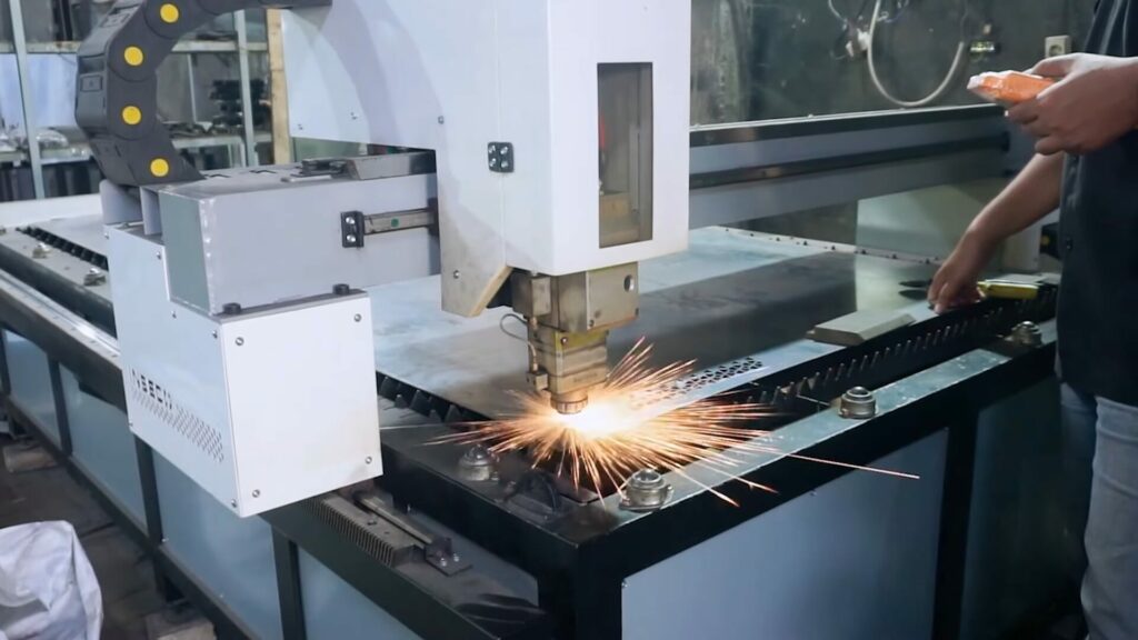 Proses pemotongan dengan mesin fiber laser CNC, menunjukkan alat laser memotong bahan logam dengan presisi tinggi dan percikan api yang dihasilkan