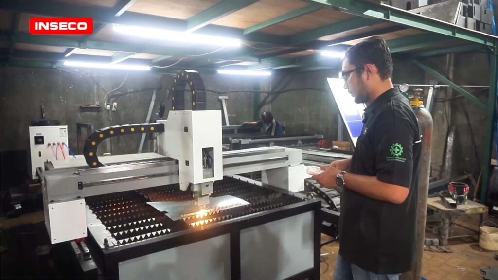 Pemandangan keseluruhan mesin laser Inseco di dalam ruangan, seorang pria berdiri di dekatnya sambil melihat hasil potongan